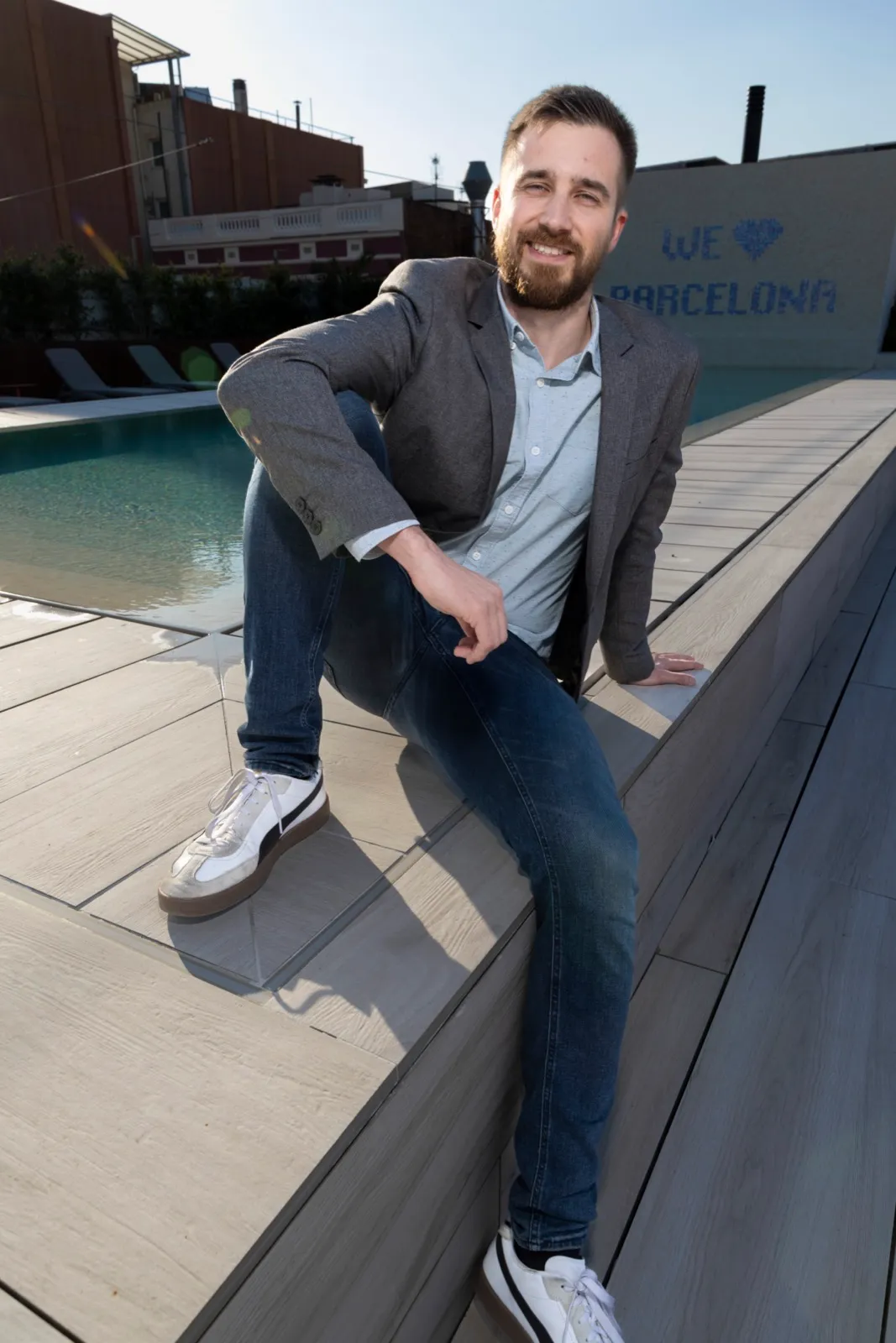 Jakob sentado al borde de una piscina en una azotea, delante de un mosaico que dice We love Barcelona, marzo de 2026.